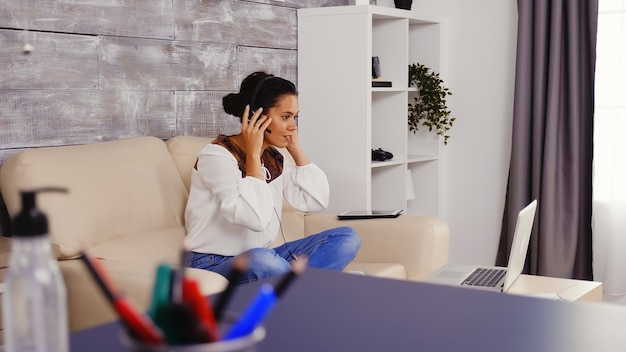 Zwolnionym tempie kobiety zakładanie słuchawek podczas rozmowy wideo przy użyciu laptopa podczas pracy w domu.