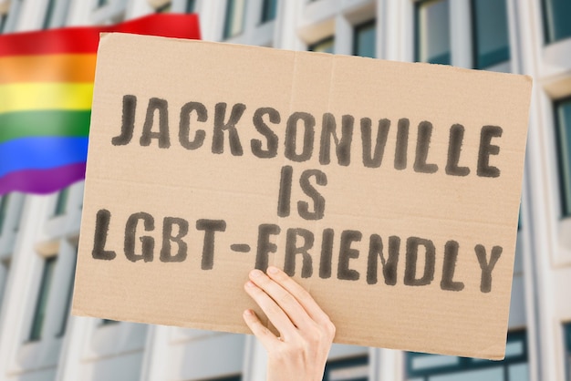 Zwrot „Jacksonville jest przyjazny dla osób LGBT” na banerze w męskiej dłoni z zamazaną flagą LGBT w tle. Relacje międzyludzkie. inny; różny. Różnorodny. wolność. Seksualność. Kwestie społeczne. Społeczeństwo