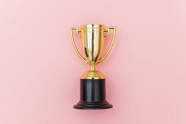 Zwycięzca lub mistrz złoty puchar trofeum na białym tle na różowym pastelowym kolorowym tle