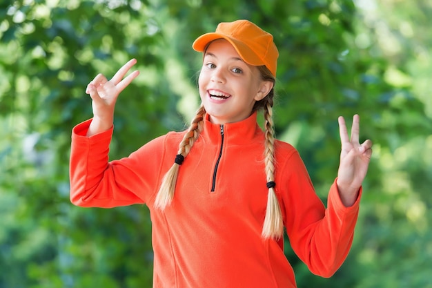 Życie jest zabawą. Szczęśliwa dziewczyna dziecko Pokaż znaki pokoju na zewnątrz. Piękny wygląd. Trend modowy. Modny styl. Opieka nad dzieckiem i dzieciństwo. Międzynarodowy Dzień Dziecka. 20 listopada.