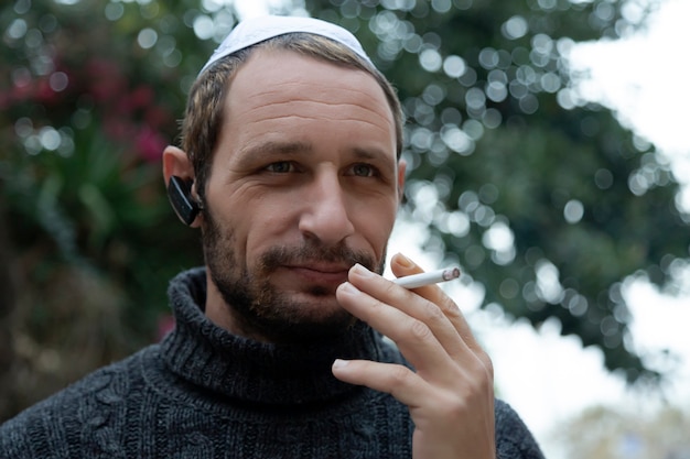 Żyd noszący słuchawkę bluetooth kippah i palący papierosa