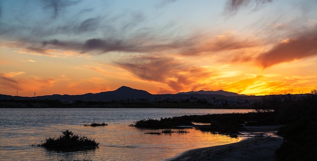 Zdjęcie Żywy zachód słońca nad solnym jeziorem na cyprze larnaca wiosną z pomarańczowym niebem i chmurami