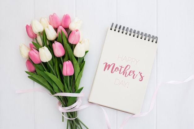 Feliz día de la madre se burla hasta en el cuaderno con tulipanes rosados y blancos, sobre fondo blanco de madera
