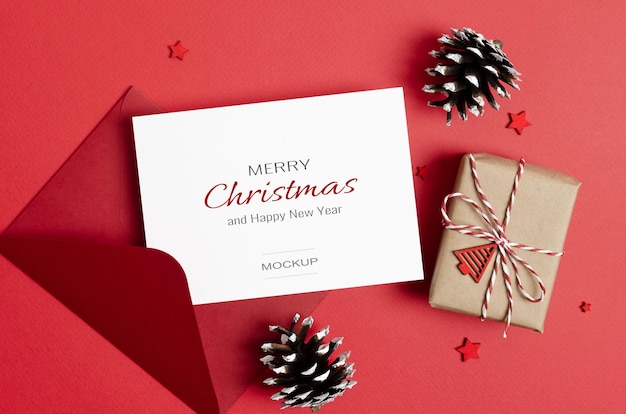 Kerstgroet of uitnodigingskaartmodel met envelop, geschenkdoos en kegelsversieringen op rood