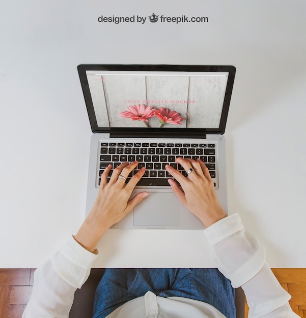 Mujer escribiendo en una computadora portátil sentada en una mesa blanca