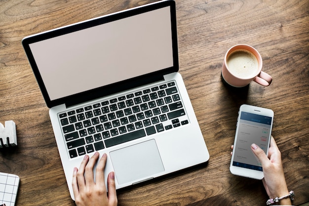 Vista aérea de la mujer que usa la computadora portátil y un teléfono inteligente en la mesa de madera