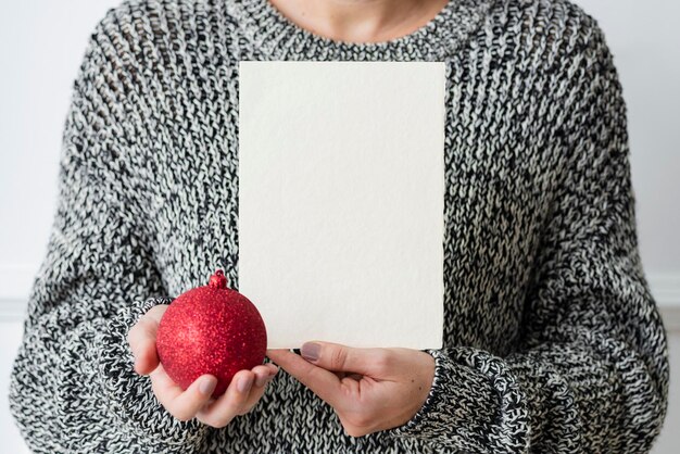 Femme tenant une boule rouge à côté d'une maquette de carte blanche
