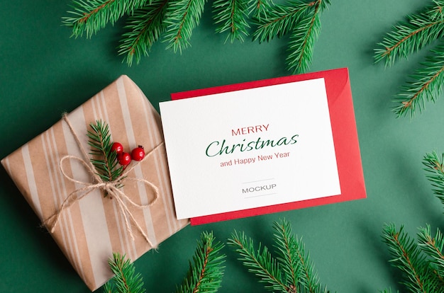 Maquette de carte de voeux de noël avec enveloppe rouge, boîte-cadeau et branches de sapin vert