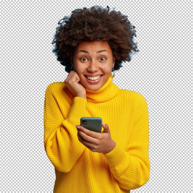 Adorável mulher adulta de pele escura vestida com um macacão amarelo usando um telefone celular com uma expressão feliz