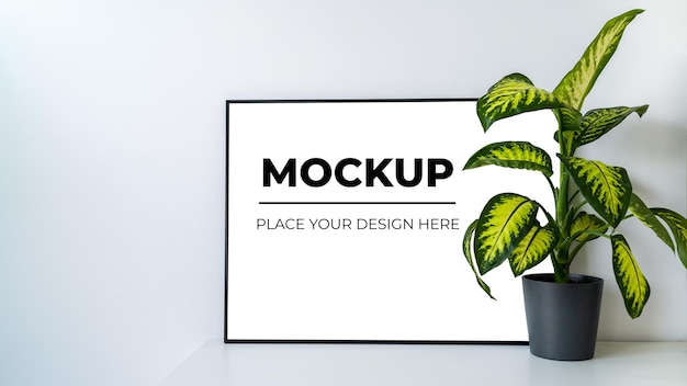 Afiche blanco en la mesa con marco negro y maqueta de plantas para tu diseño