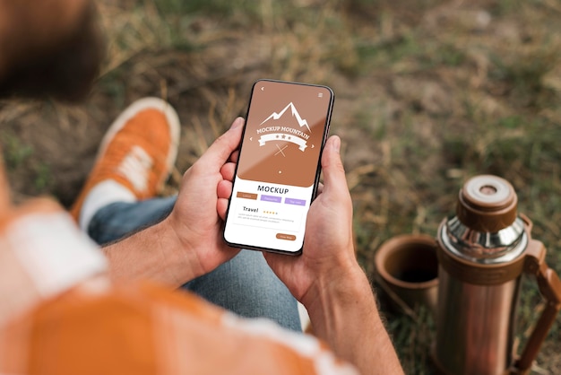 PSD alto ángulo de hombre sosteniendo smartphone mientras acampa