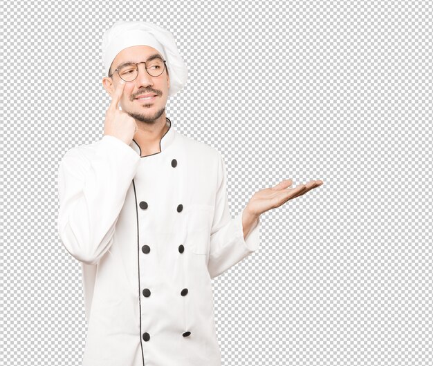 Amable joven chef haciendo un gesto de tener cuidado con su mano apuntando a su ojo