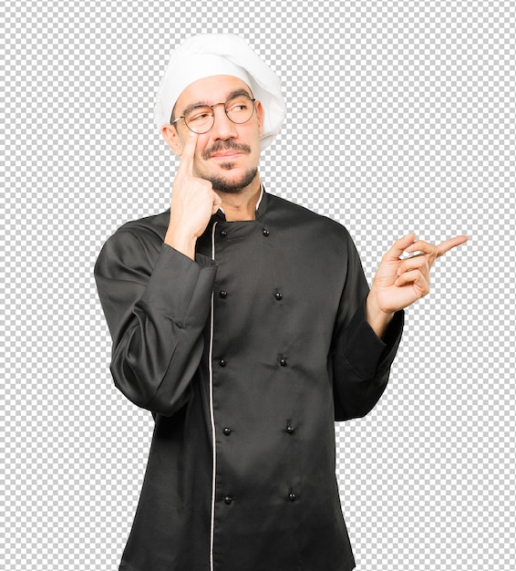 Amable joven chef haciendo un gesto de tener cuidado con su mano apuntando a su ojo