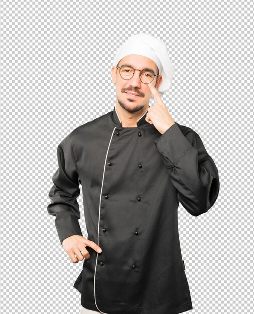 Amichevole giovane chef facendo un gesto di stare attenti con la mano che punta al suo occhio