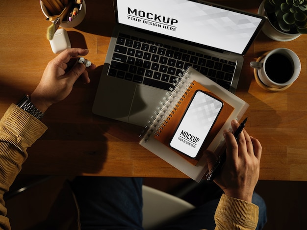 Area di lavoro con telefono digitale e mockup di laptop con tazza