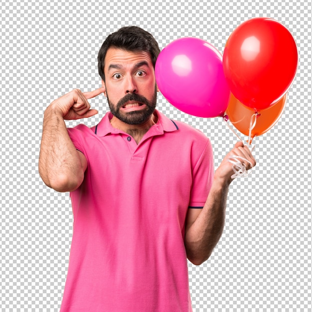 Beau jeune homme tenant des ballons et couvrant ses oreilles