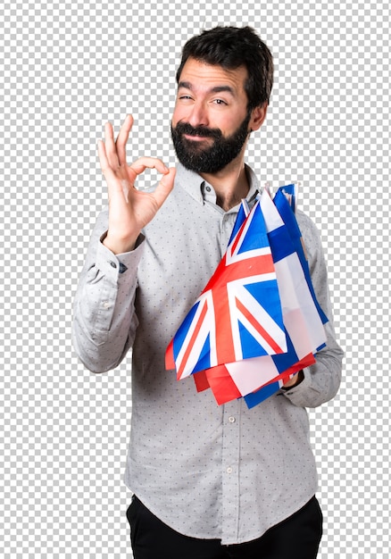 Bell&#39;uomo con la barba che tiene molte bandiere e facendo segno OK