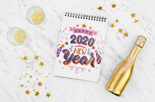 Bloc de notas blanco con cita de feliz año nuevo 2020 y botella de champán dorada