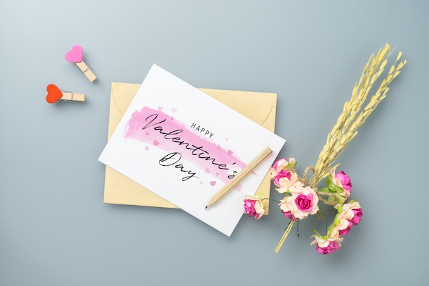 Cartolina e busta del modello sulla tavola grigia con il fiore rosa del mestiere.