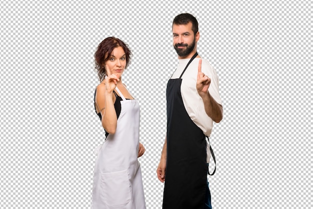 Casal de cozinheiros mostrando e levantando um dedo em sinal dos melhores