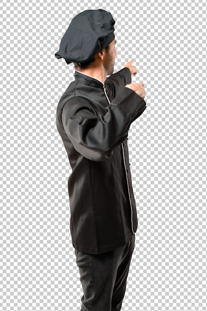 chef man in black uniform pointing back with the index finger presenting a product from behind