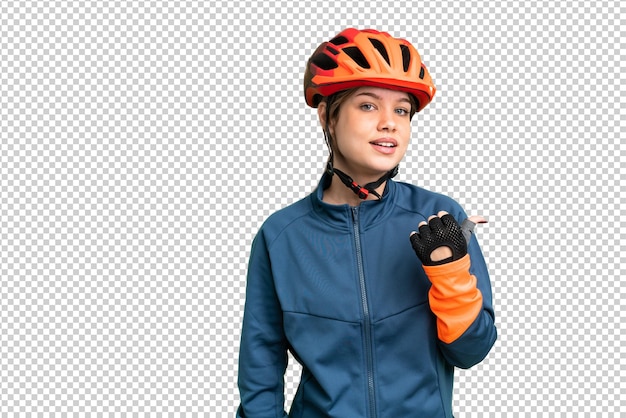 Chica ciclista joven sobre fondo de clave de croma aislado apuntando al lado para presentar un producto