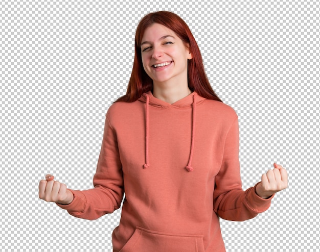 Chica joven pelirroja con sudadera rosa celebrando una victoria y feliz por haber ganado un premio