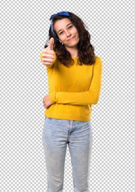 Chica joven con el suéter amarillo y pañuelo azul en la cabeza dando un gesto de pulgares arriba