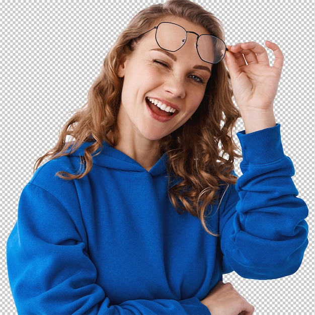 La chica rubia afortunada sonriendo mirando despreocupada y guiñando el ojo a las gafas de despegue de la cámara de pie con capucha contra un fondo blanco