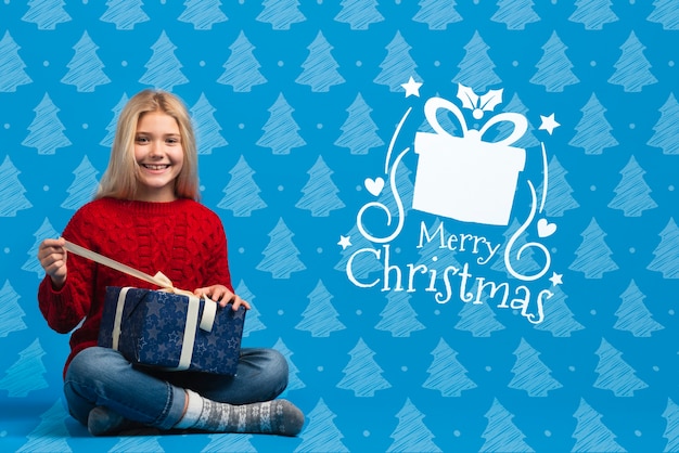 Chica vestida con suéter temático de Navidad abriendo regalo