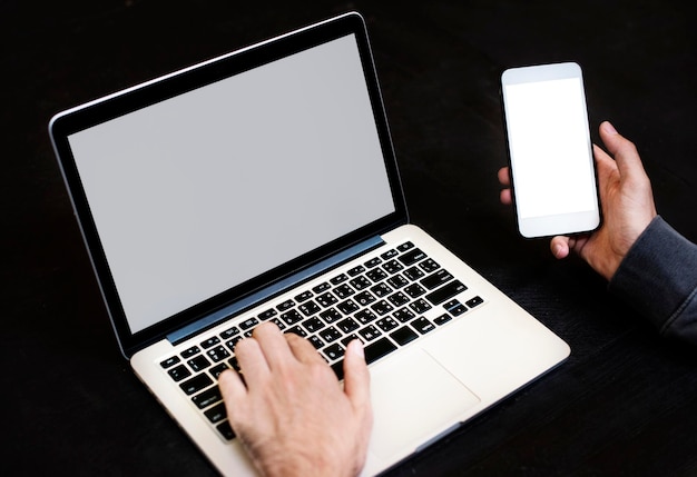 Close-up di una mano che tiene un telefono cellulare con lo sfondo di un computer portatile