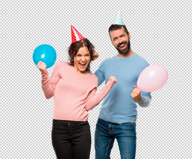 Coppia con palloncini e cappelli di compleanno che celebra una vittoria e felice per aver vinto un premio