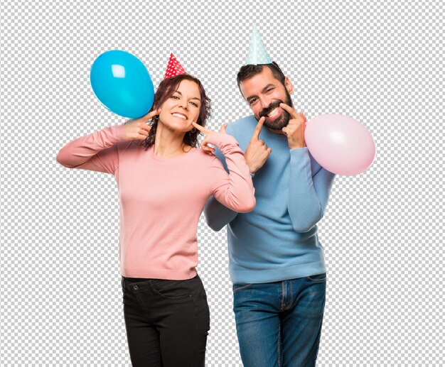 Coppia con palloncini e cappelli di compleanno sorridenti con una piacevole espressione