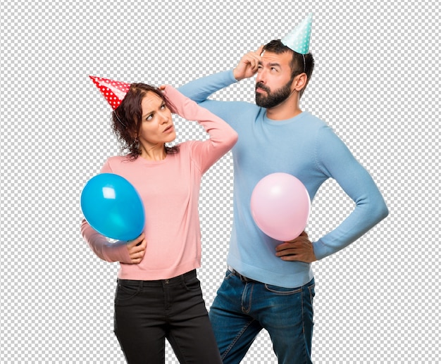 Couple avec des ballons et des chapeaux d&#39;anniversaire ayant des doutes et avec un visage confus en se grattant la tête