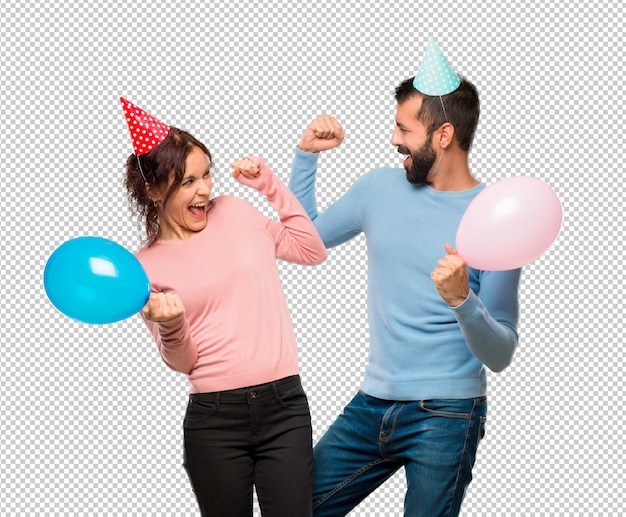 Couple avec des ballons et des chapeaux d&#39;anniversaire célébrant une victoire en position gagnante