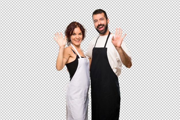 Couple de cuisiniers saluant avec la main avec une expression heureuse