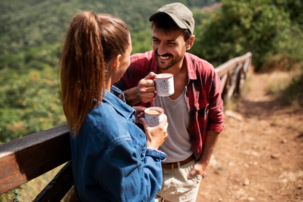 PSD couple tenant des tasses tout en voyageant ensemble dans la nature