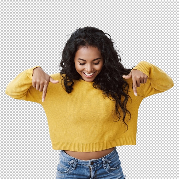 Curiosa e intrigada bonita feminina afro-americana garota de camisola amarela apontando e olhando para baixo com sorriso divertido verificando promoção incrível olhando para a publicidade parede branca