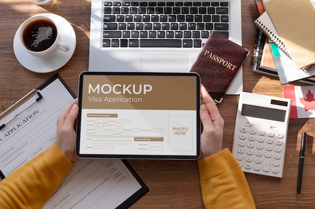 Domanda di visto mock up in tablet tenuto da mani umane sulla scrivania con passaporto, laptop e documenti