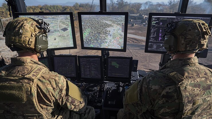 PSD dos soldados con uniformes de camuflaje militar que operan múltiples monitores que muestran mapas aéreos y datos tácticos en la cabina de un vehículo