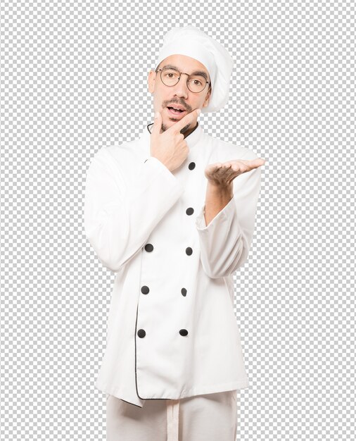 Dudoso joven chef sosteniendo algo con su mano