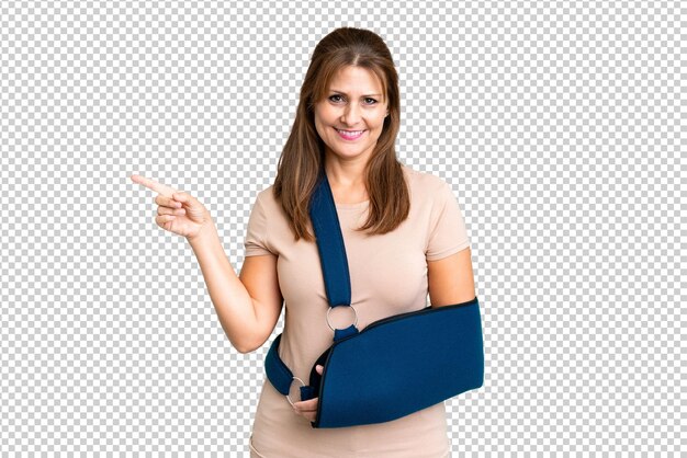 Edad media con un brazo roto y un cabestrillo sobre un fondo aislado que señala con el dedo al costado