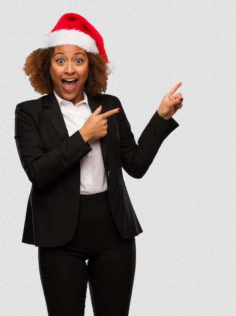 Empresaria negra joven que lleva un sombrero de santa de la Navidad que lleva a cabo algo con la mano