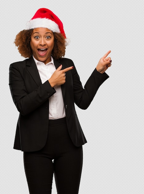 Empresaria negra joven que lleva un sombrero de santa de la navidad que lleva a cabo algo con la mano