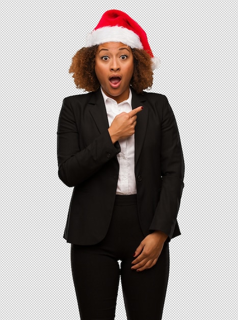 Empresaria negra joven que lleva un sombrero de santa de la Navidad que señala al lado