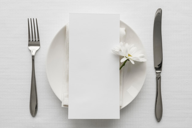 Endecha plana de la maqueta del menú de primavera en un plato con cubiertos y flor