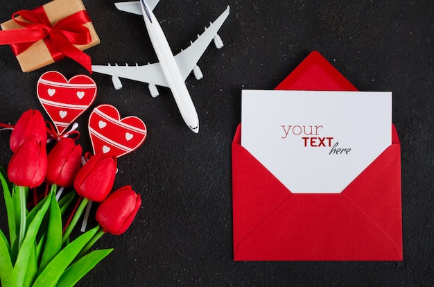 Enveloppe rouge avec papier vierge, modèle d'avion, bouquet de tulipes et coffret cadeau avec coeurs