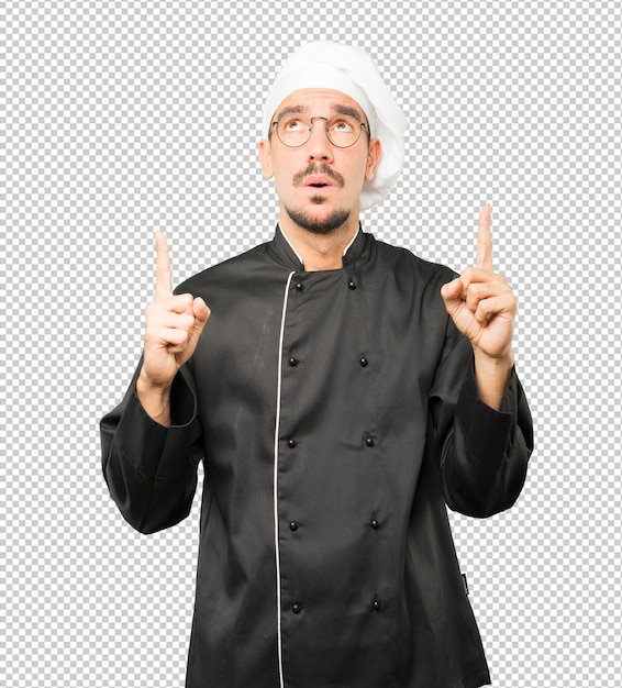 Esitante giovane chef rivolto verso l'alto con il dito