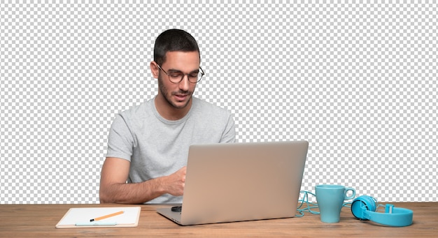 Felice giovane uomo seduto alla sua scrivania e usando il suo computer portatile