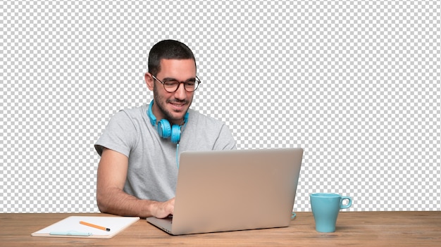 Felice giovane uomo seduto alla sua scrivania e utilizzando una cuffia